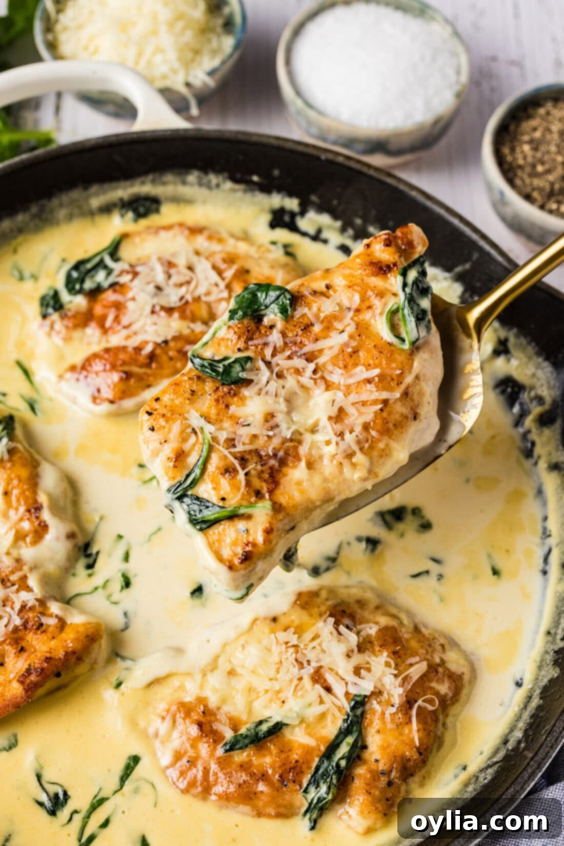 Spatula holding up a piece of Chicken Florentine above a skillet, showcasing golden chicken and creamy spinach sauce
