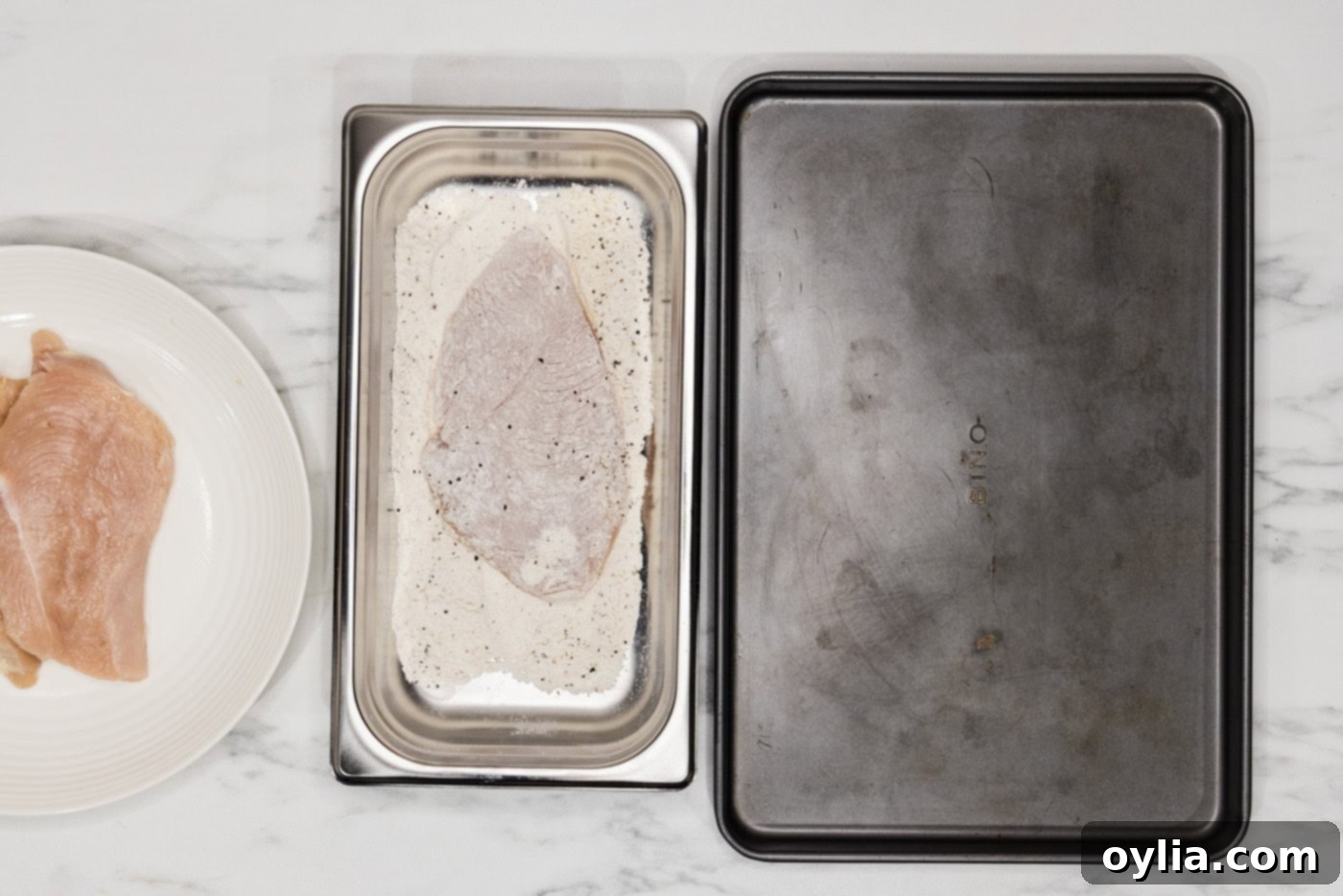 chicken cutlet being pressed into a flour mixture in a breading tray for coating
