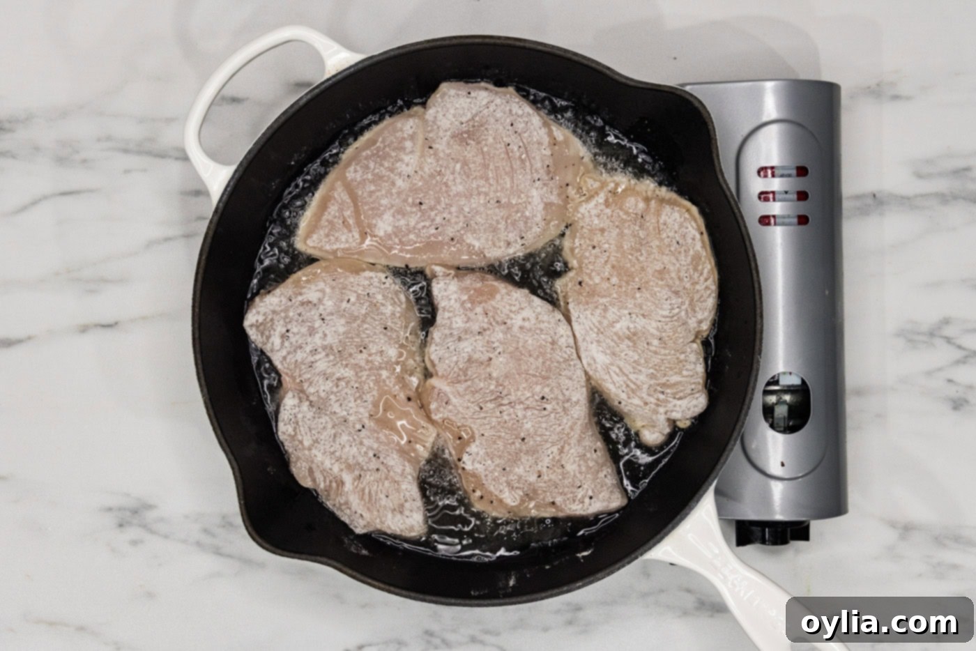 lightly coated chicken cutlets searing in a cast iron skillet on the stovetop