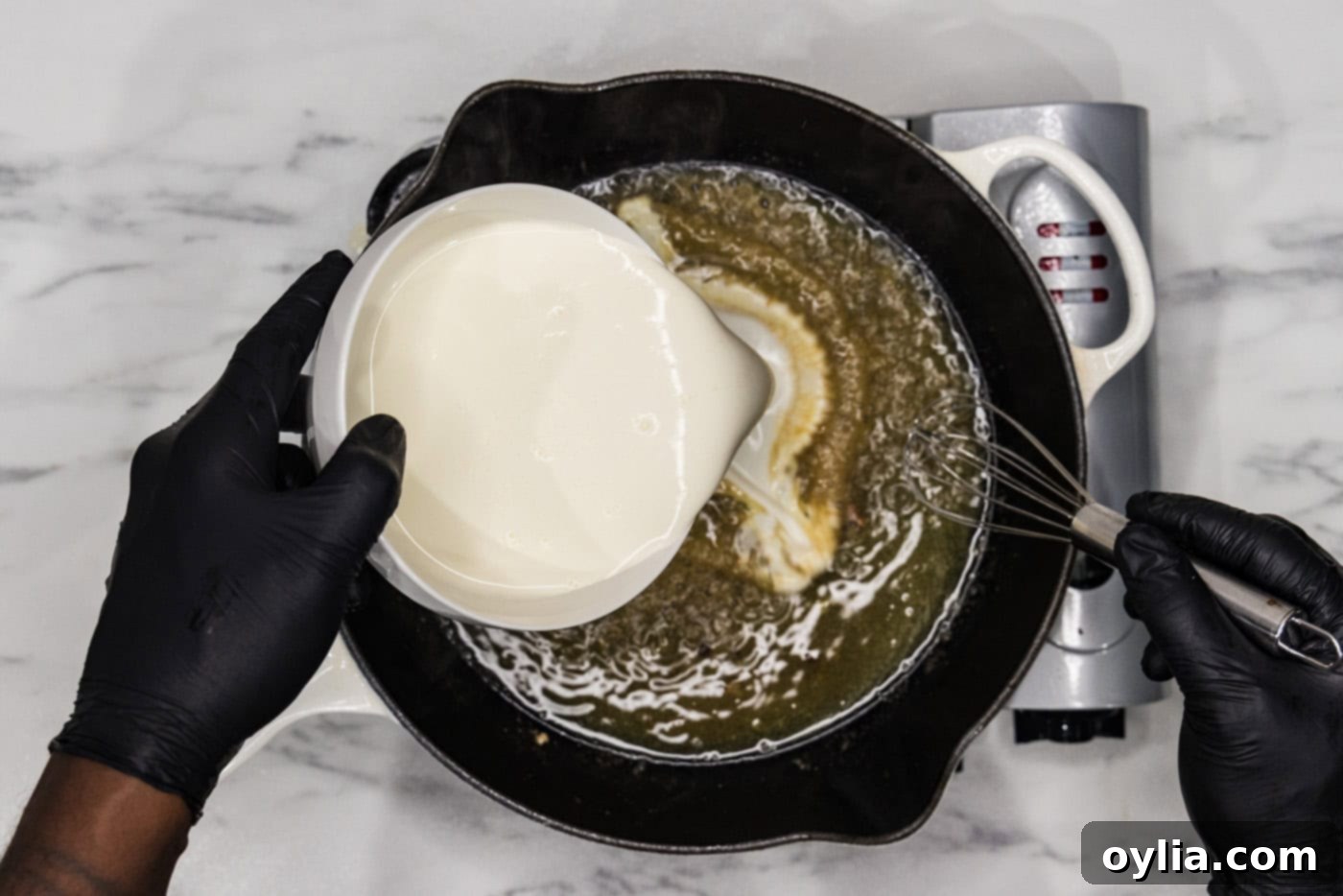 pouring heavy cream into a skillet with a simmering broth mixture