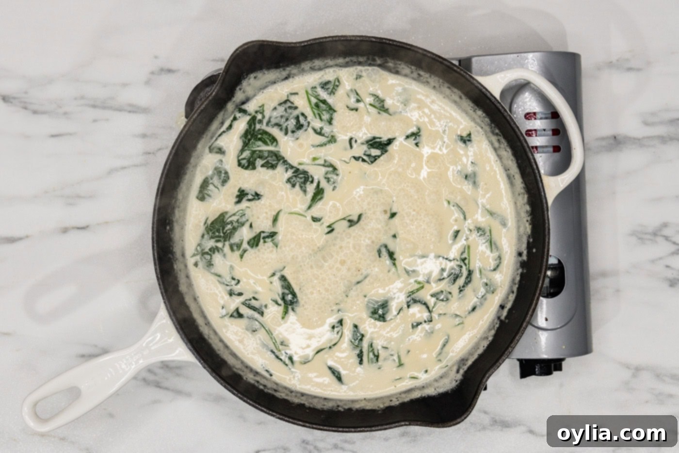 fresh spinach leaves wilting in a creamy sauce in a skillet
