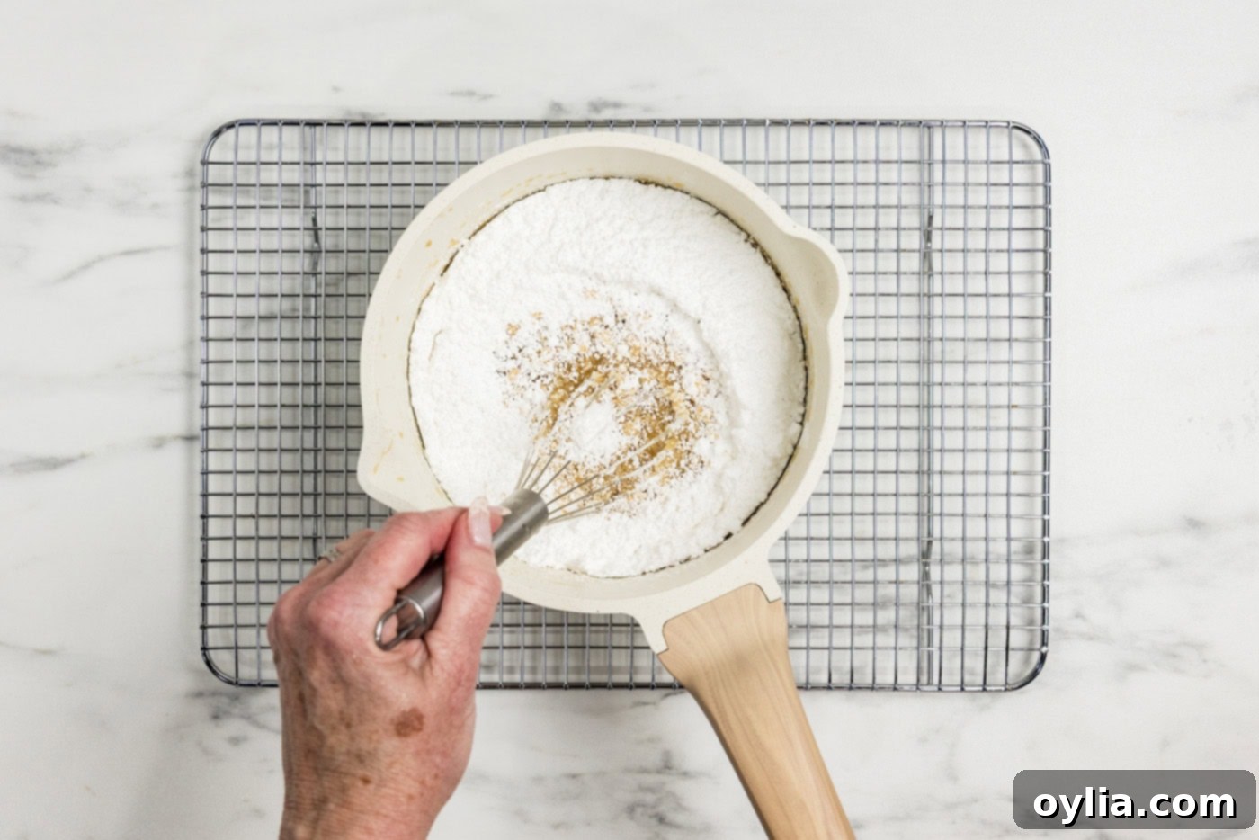 whisking powdered sugar in a saucepan of caramel icing