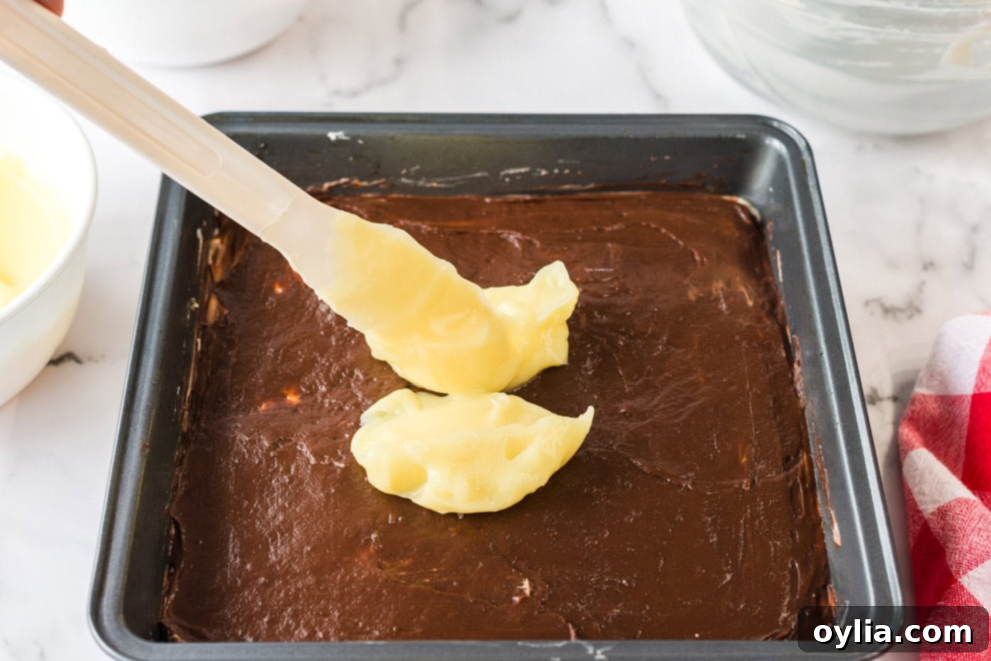 Creamy vanilla pudding being dolloped and spread over the chocolate pudding layer in the baking pan, completing the pudding section.