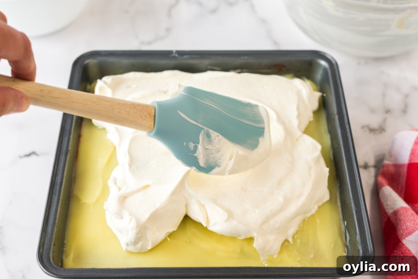 The remaining fluffy Cool Whip being gently spread over the vanilla pudding layer, creating the final, airy topping for the dessert.