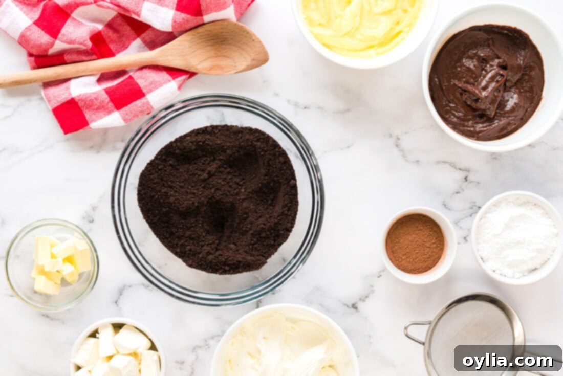 A selection of ingredients laid out on a counter, including a block of cream cheese, butter, packages of instant pudding, a tub of whipped topping, and chocolate graham crackers.