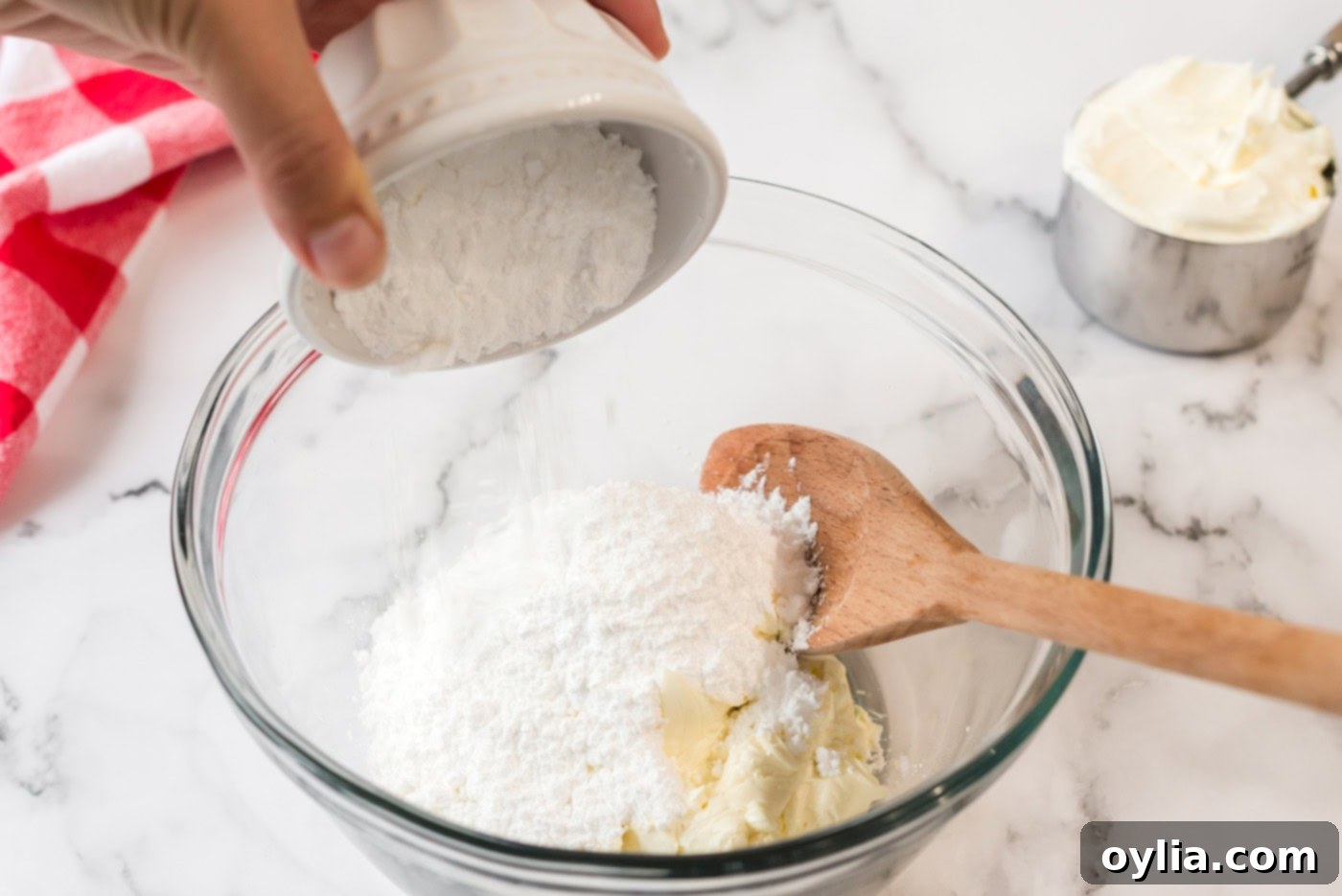 Powdered sugar being added to a bowl of softened cream cheese, ready to be beaten into a creamy mixture for the dessert's second layer.