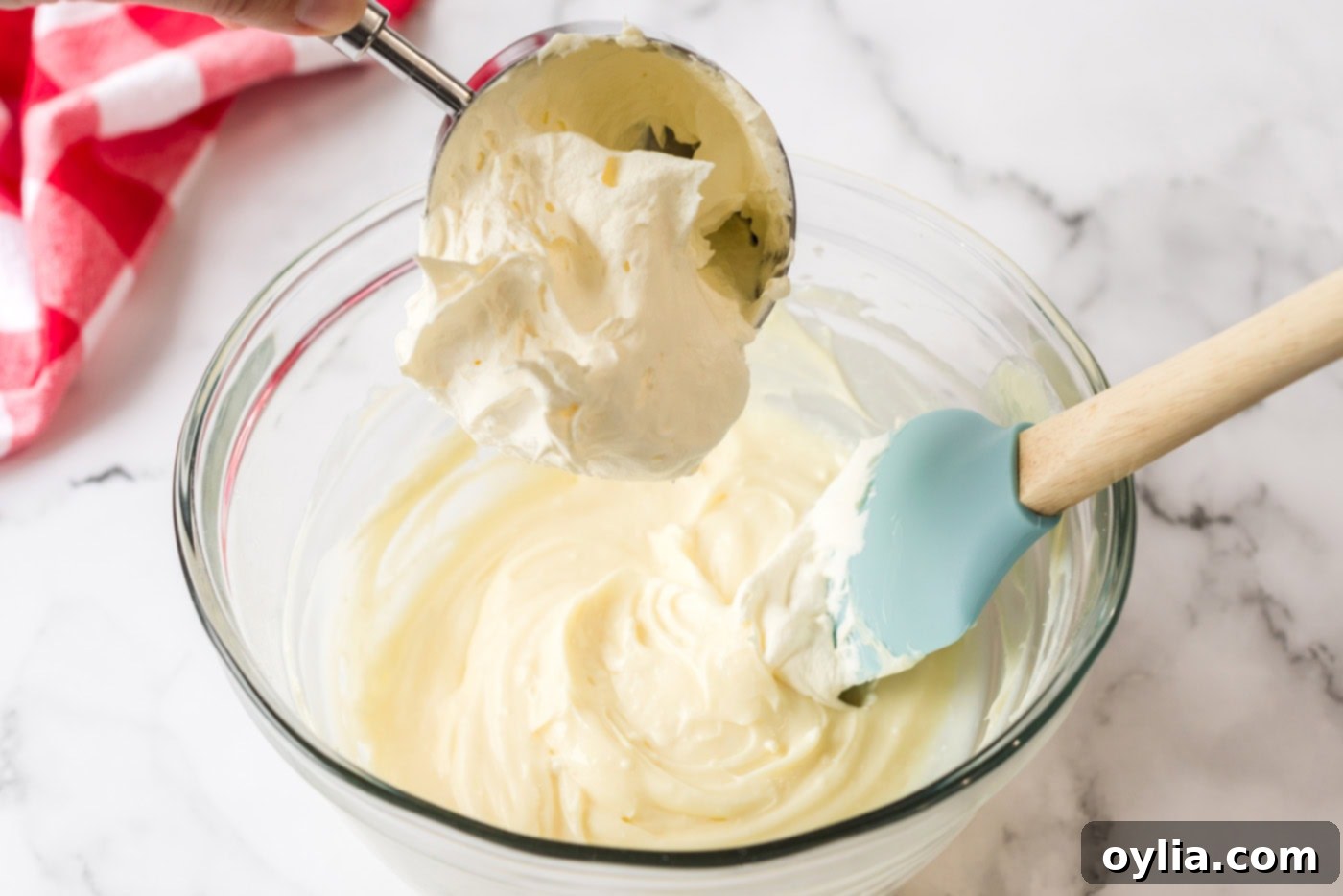 A dollop of Cool Whip being carefully folded into the smooth cream cheese mixture using a rubber spatula, preparing it for the dessert layers.