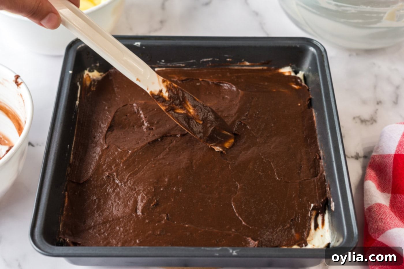 Smooth chocolate pudding being evenly spread over the cream cheese layer in the baking pan, forming the next delicious layer.
