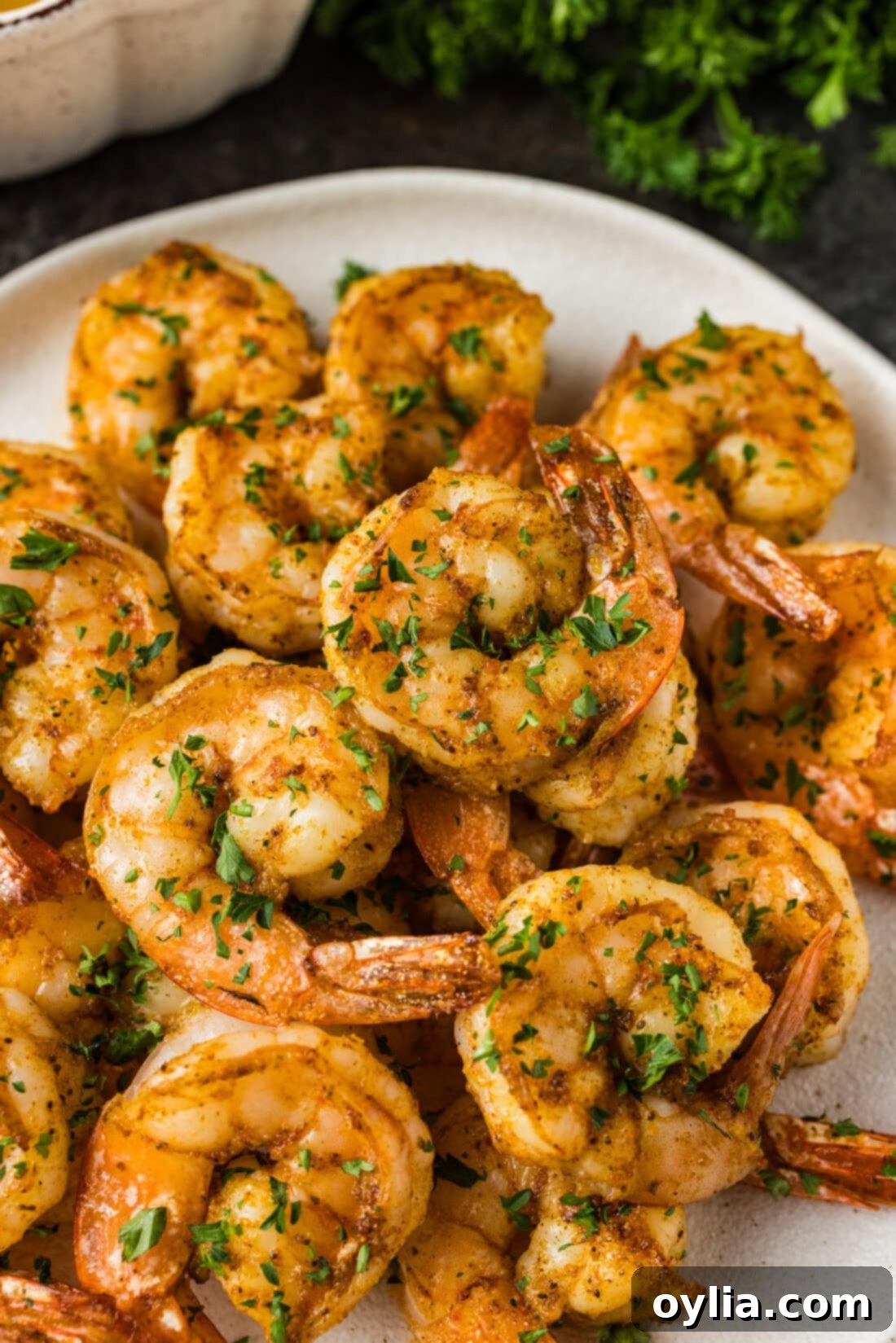 Close up photo of perfectly cooked Broiled Shrimp on a white plate, garnished with fresh herbs