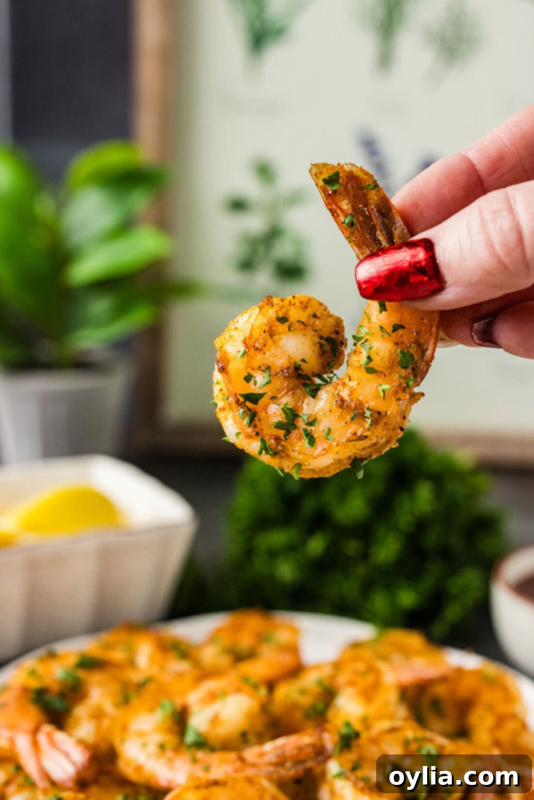 A hand holding a single piece of perfectly broiled shrimp, showing its pink color and curl