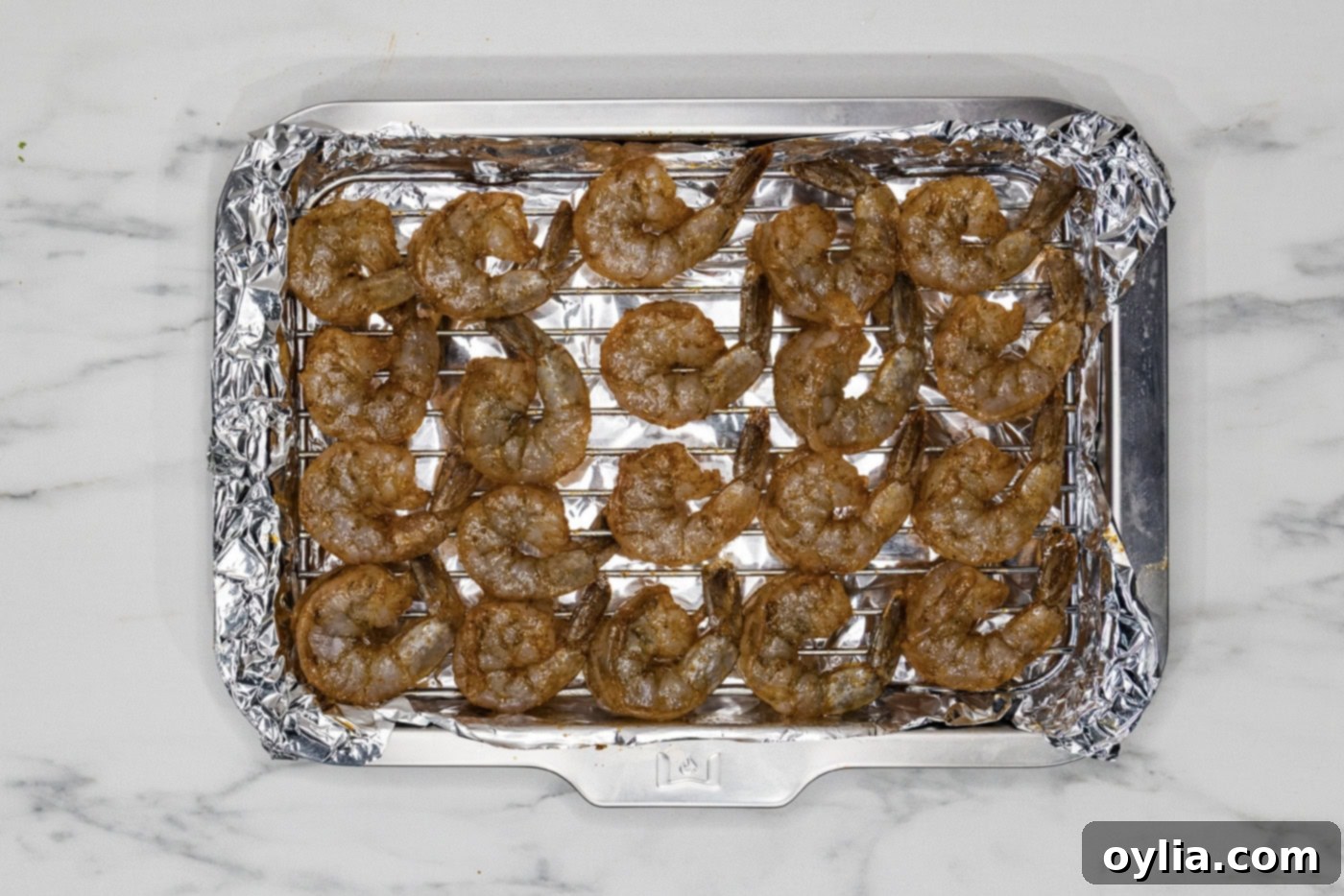Seasoned raw shrimp neatly arranged in a single layer on a wire rack over a foil-lined baking sheet, ready for the broiler