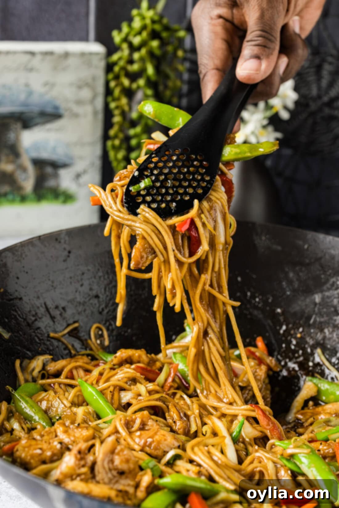 Tongs lifting Chicken Lo Mein out of a wok
