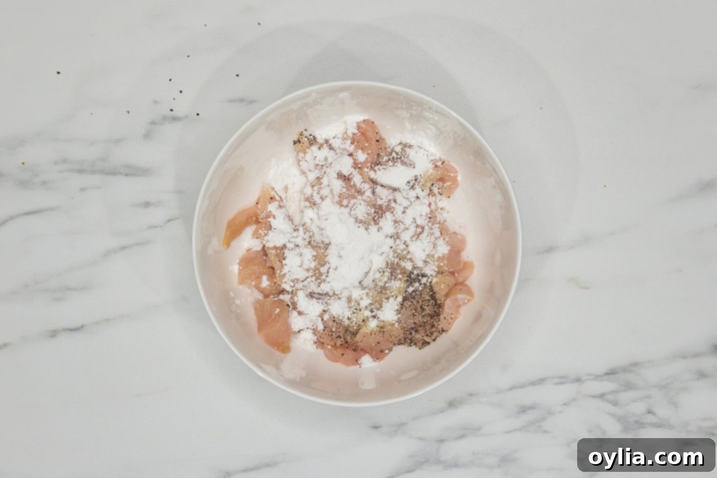 raw chicken pieces in a bowl with cornstarch and seasonings