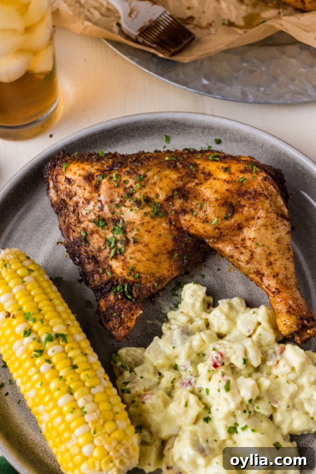 Perfectly Smoked Chicken Quarters 3 Close up photo of a Smoked Chicken Quarter on a plate with potato salad and corn on the cob, showcasing its beautiful golden-brown skin and juicy texture.