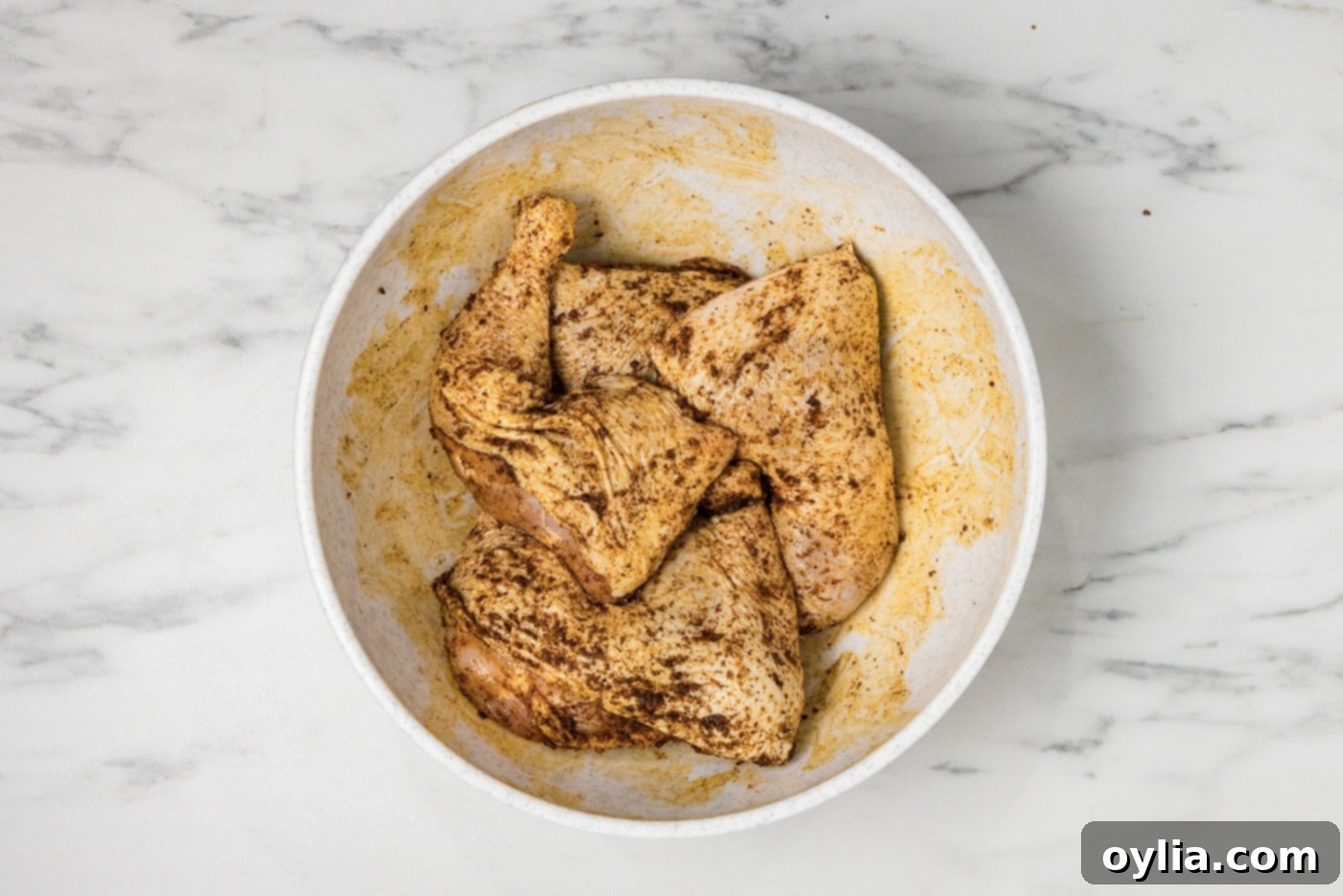 Raw chicken quarters in a bowl with wet rub, showing the seasoning being applied before smoking.