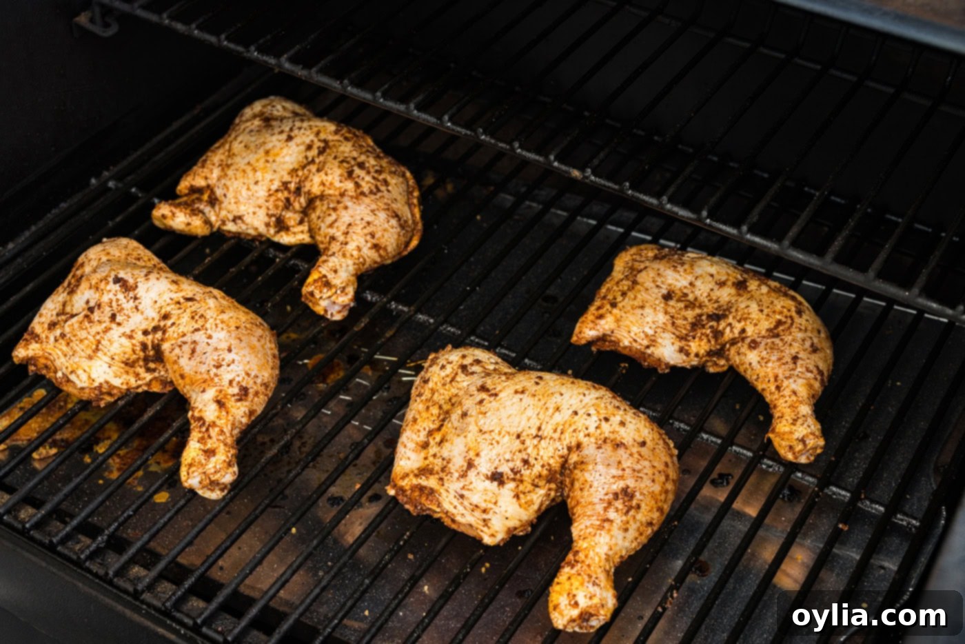 Photo of seasoned chicken quarters on smoker grill grates, showing multiple pieces cooking slowly.