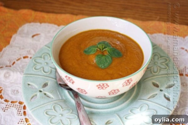 A close up photo of a bowl of pumpkin soup with a spoon on the side.