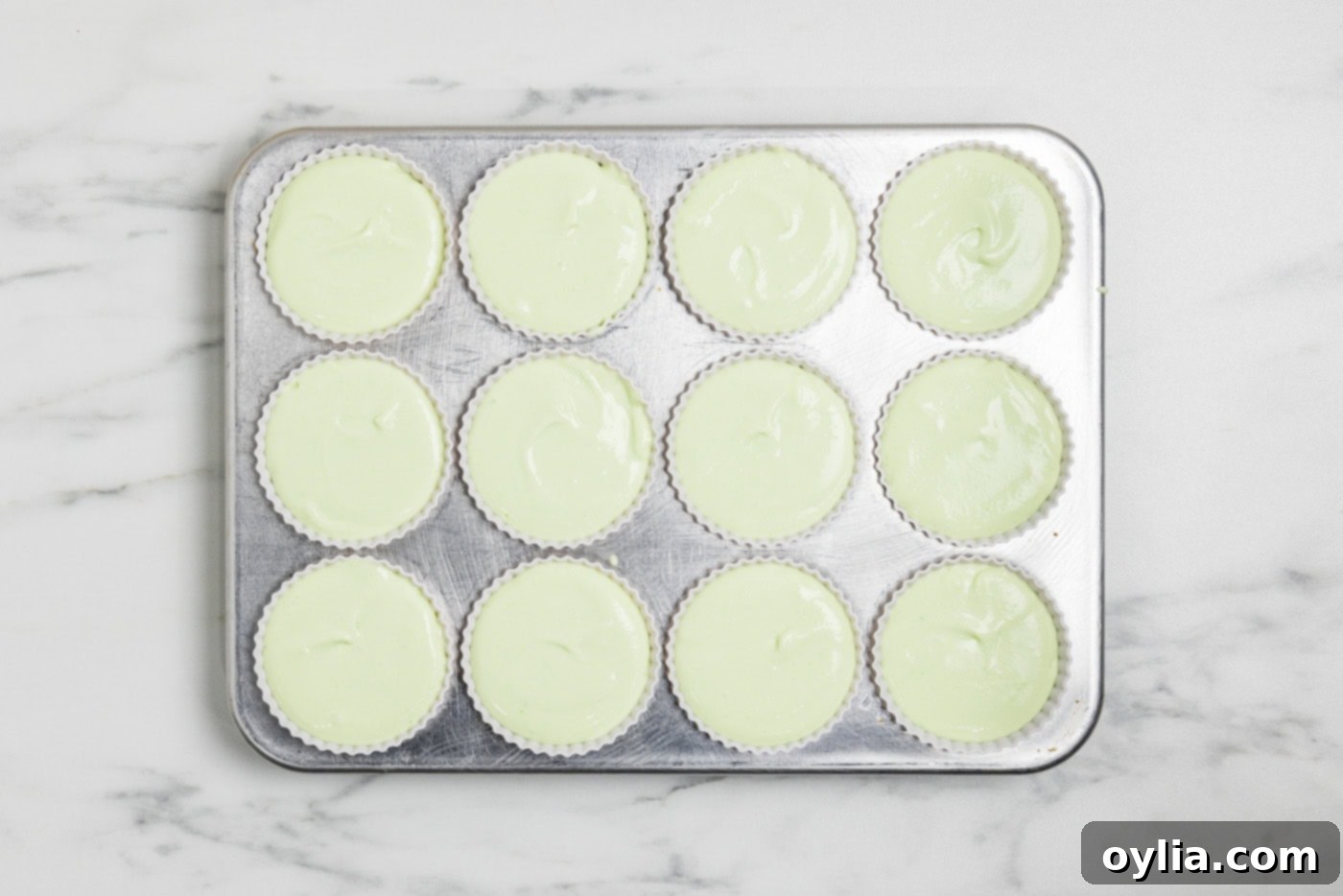 Overhead photo of cheesecake mixture in silicone baking cups, neatly placed inside a muffin pan.