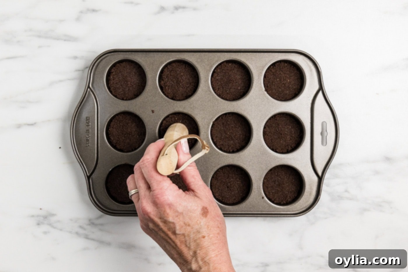 Hand using a pestle to push down graham cracker crust in a mini cheesecake pan