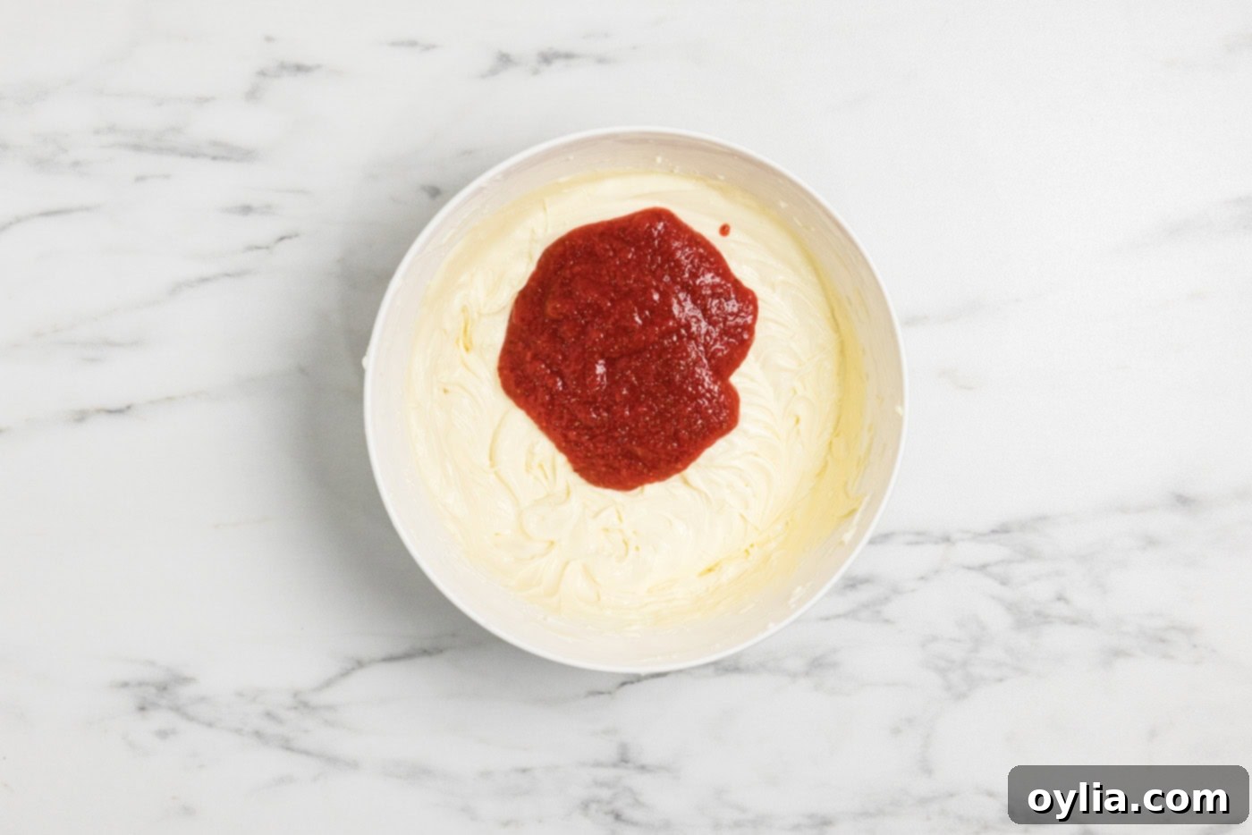 strawberry compote added to cheesecake batter in a bowl