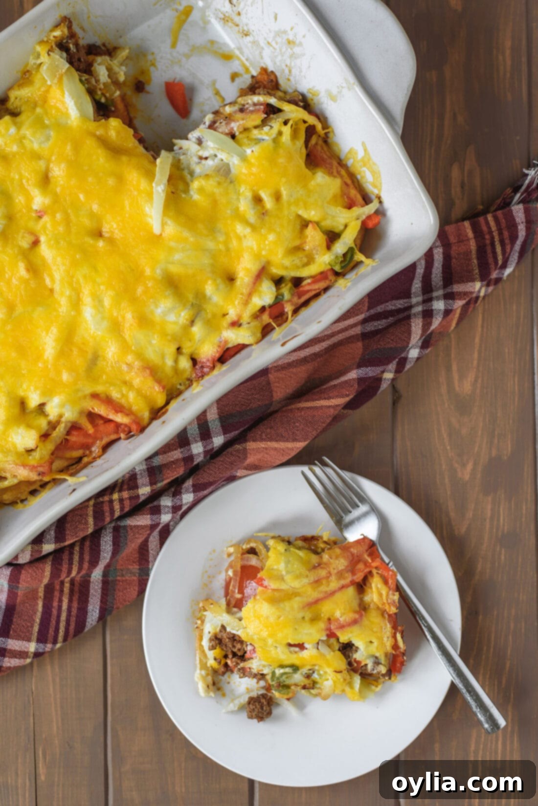 A serving of John Wayne Casserole on a plate next to the baking pan, showing its delicious layers of beef, cheese, and vegetables on a golden biscuit crust.