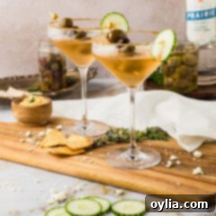 Two Dirty Greek Martinis on a wooden platter with olives and cucumber.