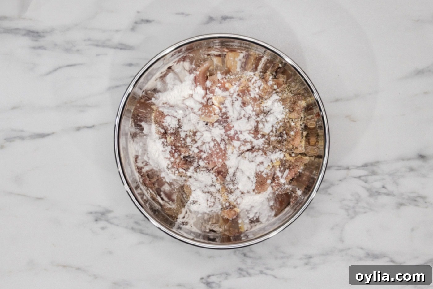 Sliced chicken in a bowl with cornstarch sprinkled on top, ready for coating.