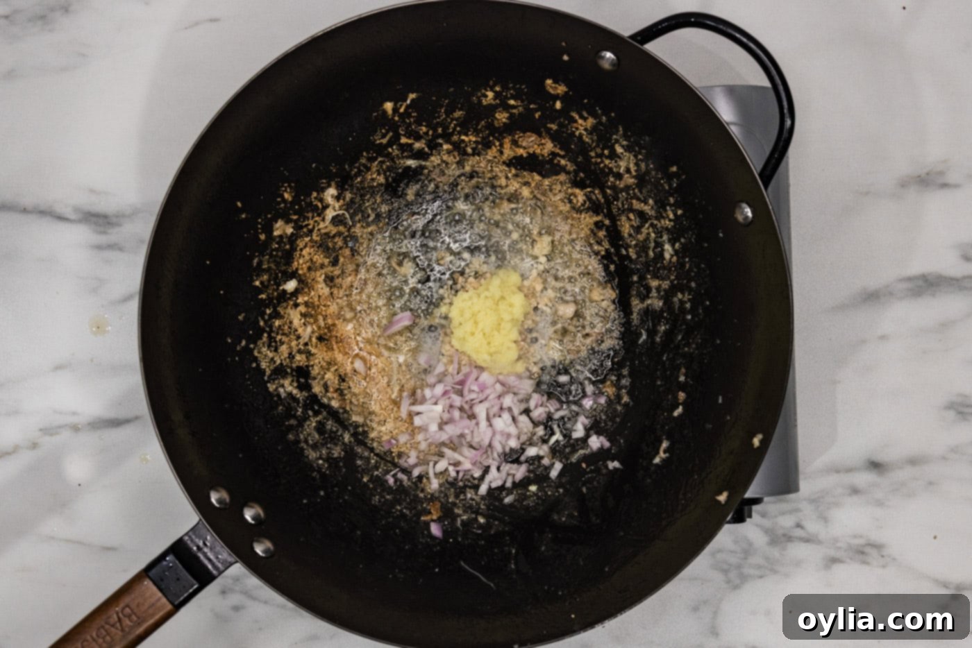 Minced garlic, ginger, and chopped shallots added to a hot wok, releasing their fragrance.