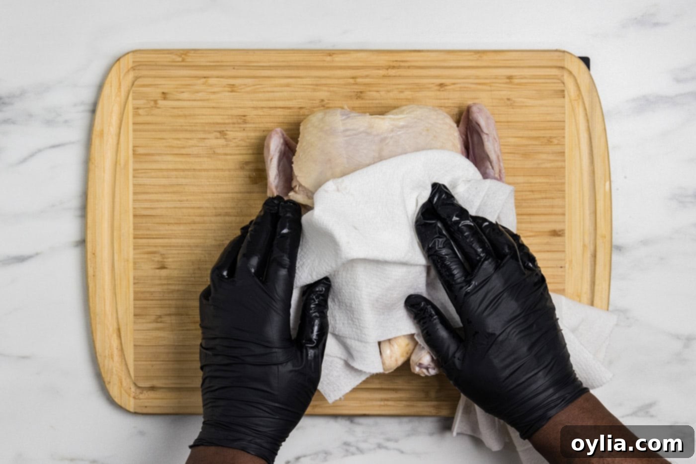 hands patting whole raw chicken dry with paper towels