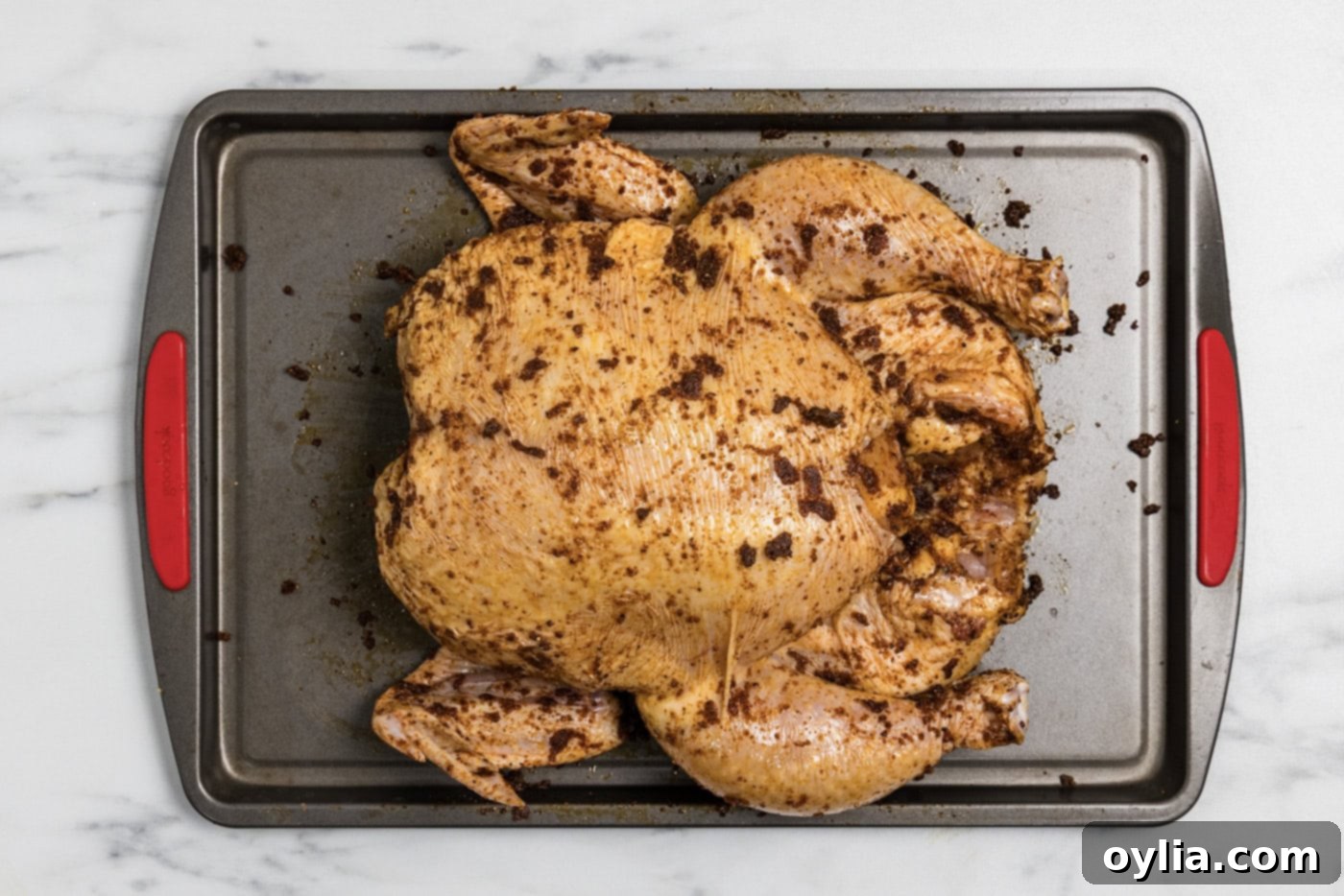 whole raw chicken coated in oil and spice rub on a baking sheet