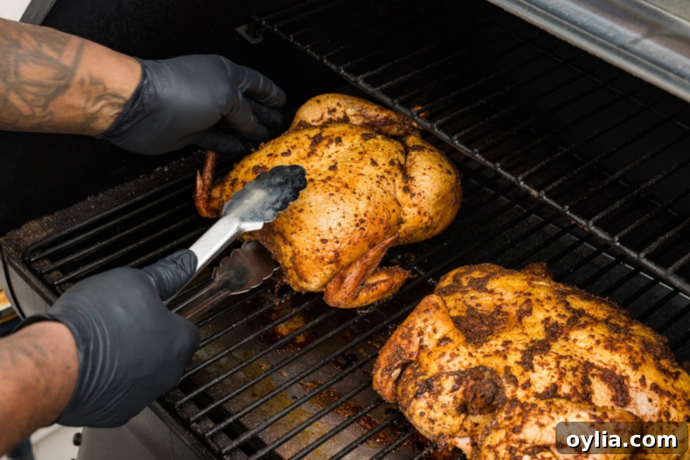 tongs flipping whole chicken upside down on a smoker grate
