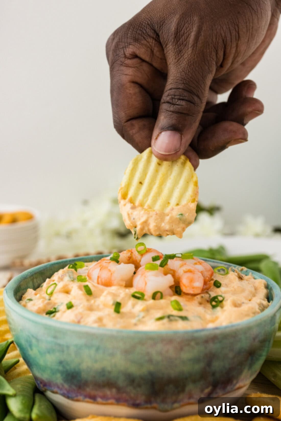 Hand holding a chip generously dipped in creamy shrimp dip, ready to eat