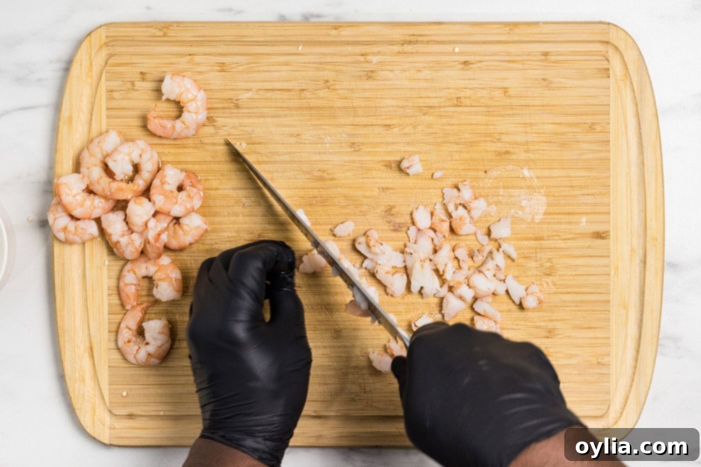 Hands using a knife to chop up cooked shrimp on a cutting board into small, even pieces