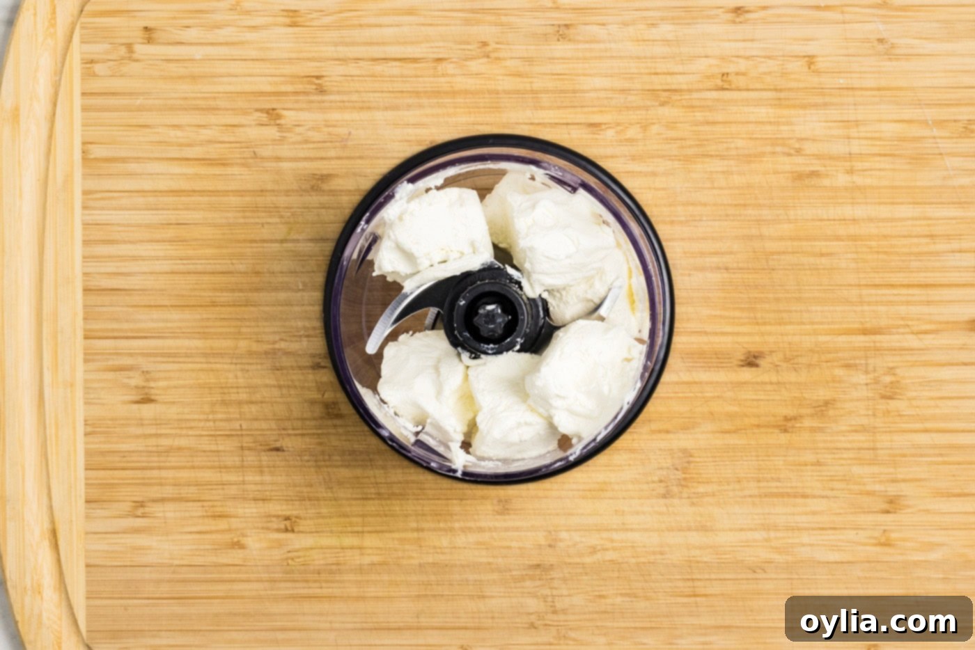 cubed cream cheese in the bowl of a mini food chopper, ready for blending