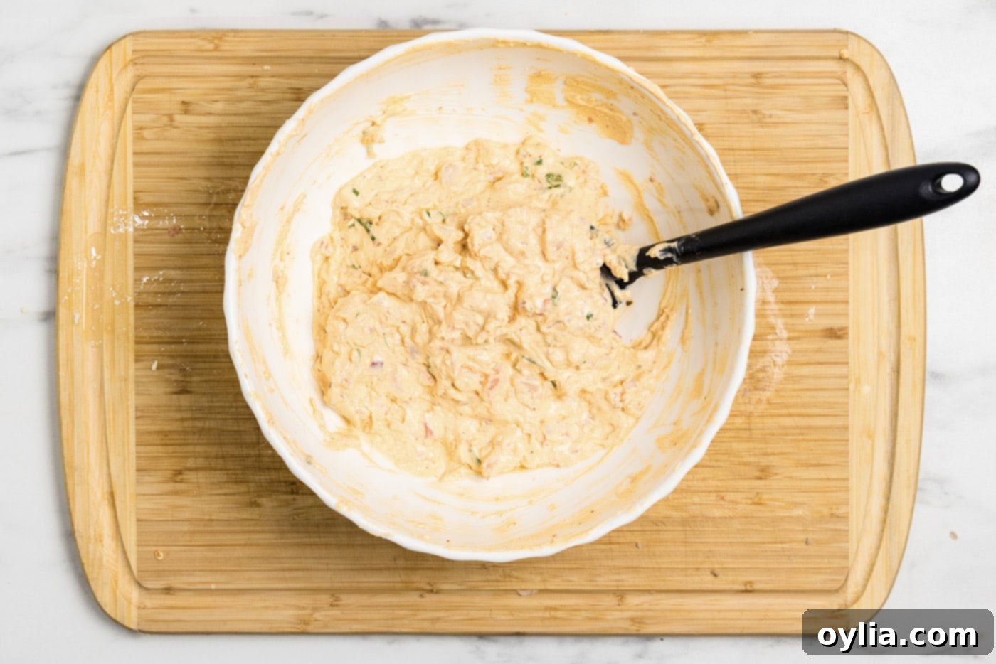 Rubber spatula in a bowl of mixed shrimp dip, illustrating its creamy texture before chilling