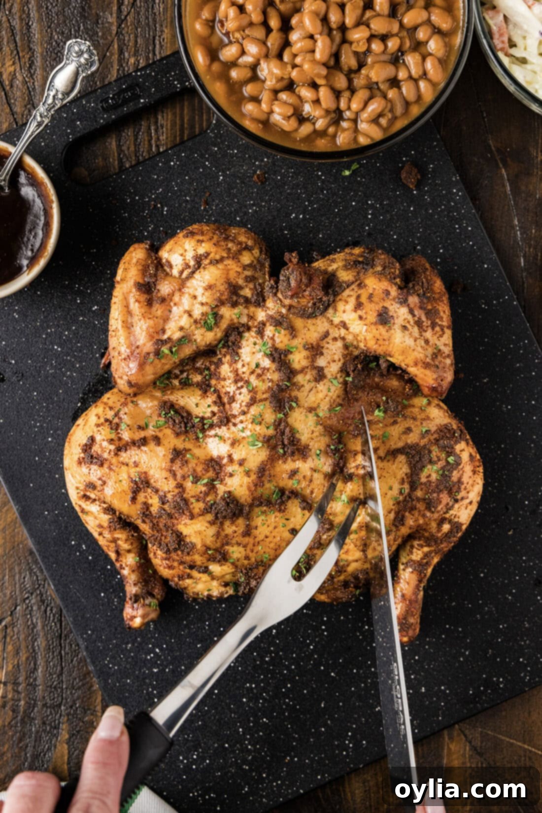 Smoked Spatchcock Chicken on a black board being carved with a fork and knife, showcasing its tender meat.