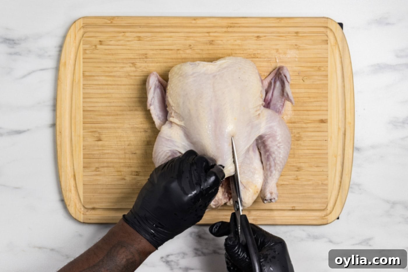Using kitchen shears to cut along a whole raw chicken's back, a key step for spatchcocking.