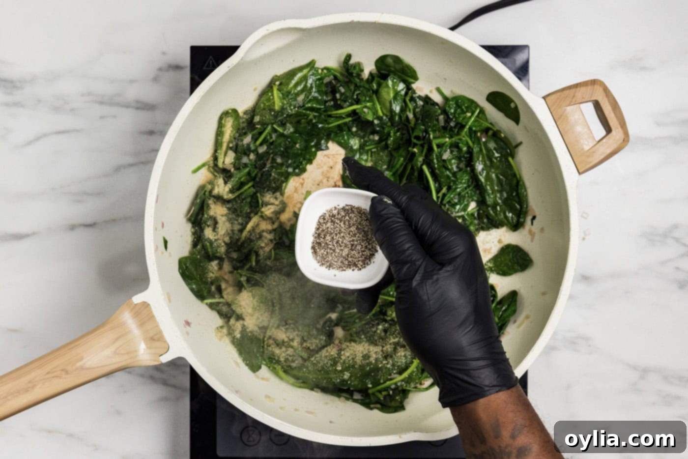 overhead photo of hand adding black pepper to spinach mixture in. skillet