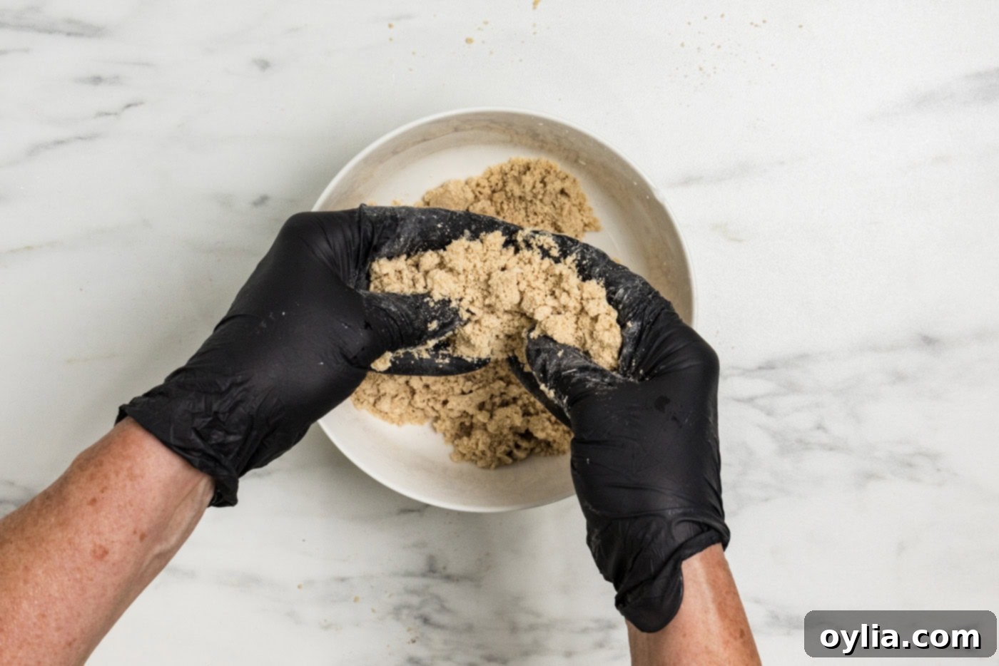 gloved hands squeezing streusel ingredients together in a bowl
