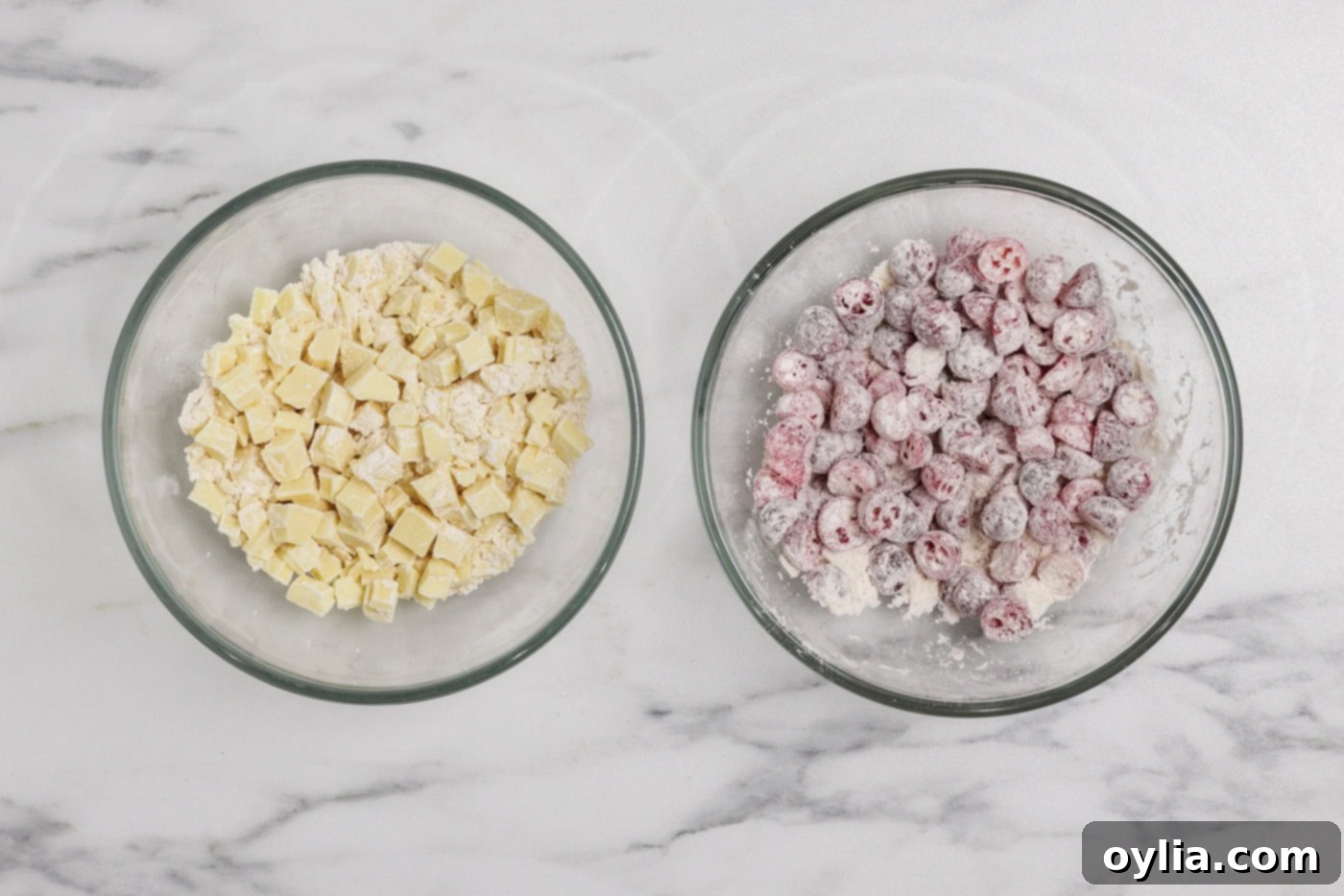 Frozen cranberries and chopped white chocolate coated in flour mixture in separate bowls, ready for baking.