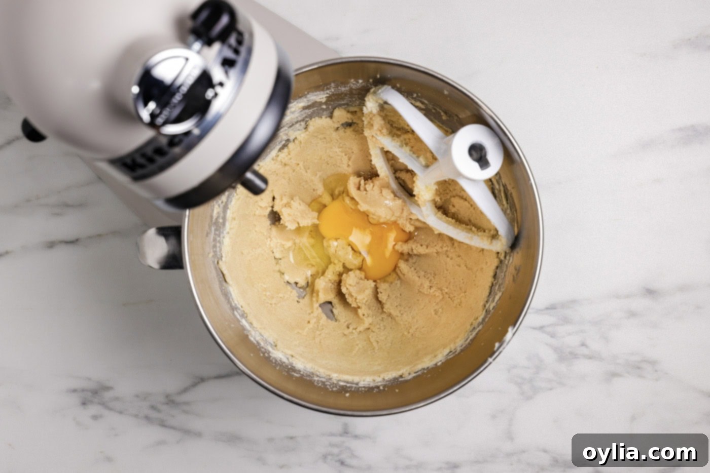 Adding eggs to the creamed sugar and butter mixture in a stand mixer bowl, for a smooth muffin batter.