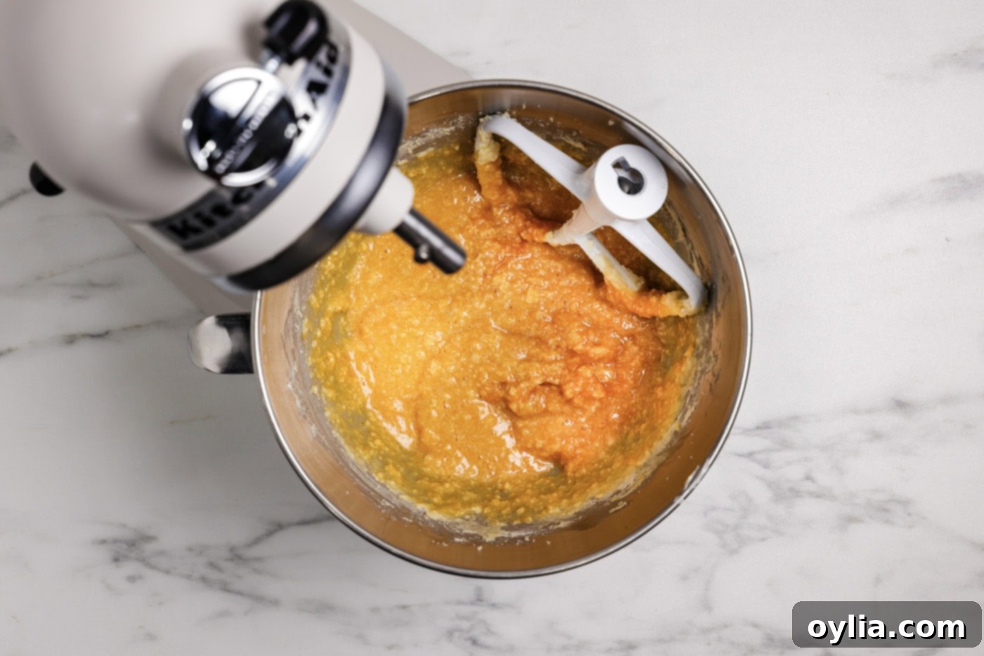 Pumpkin and buttermilk mixture being incorporated into the wet ingredients in a stand mixer bowl.