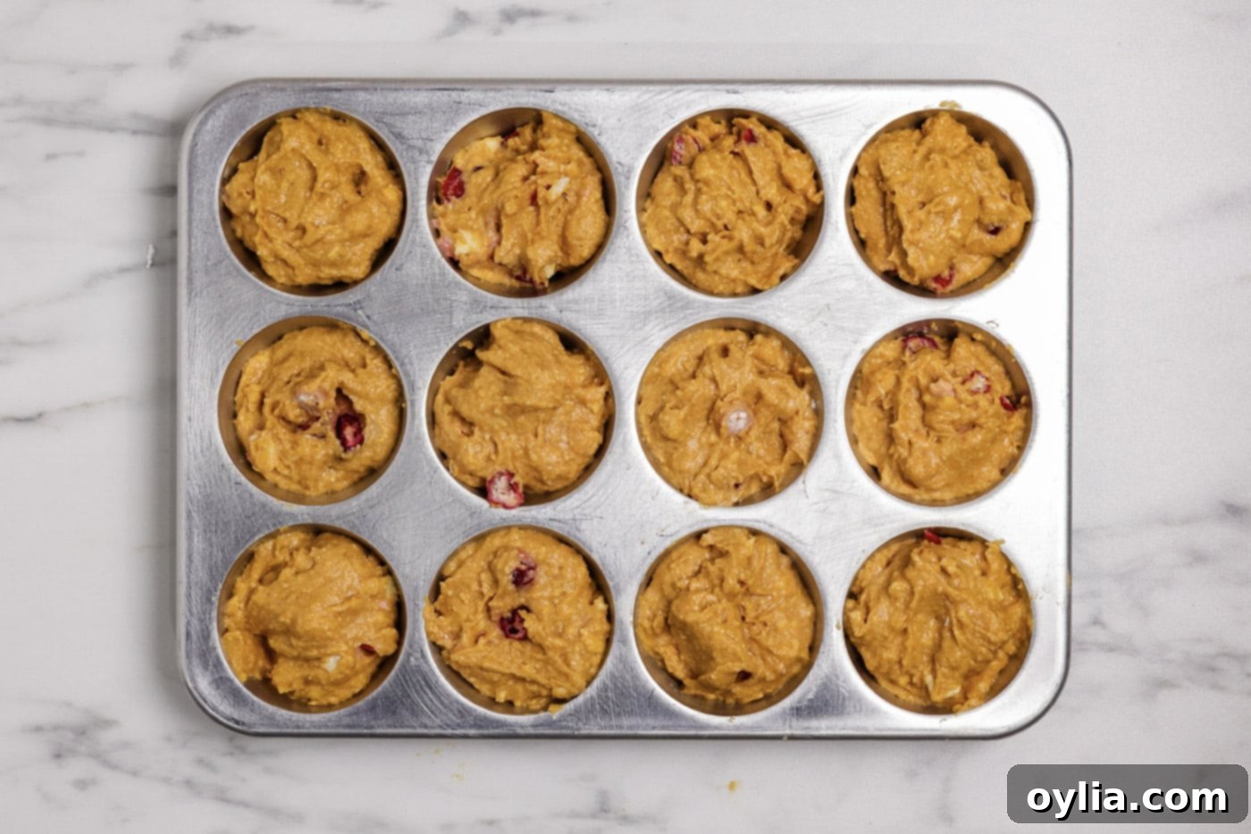 Pumpkin cranberry muffin batter scooped into a muffin pan, ready for baking.