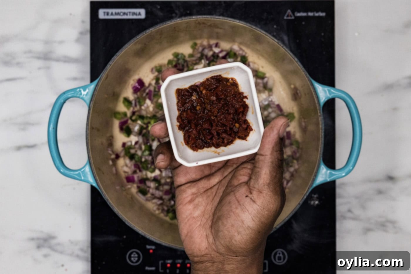 hand holding a bowl of chopped chipotle peppers over dutch oven with sauteed vegetables