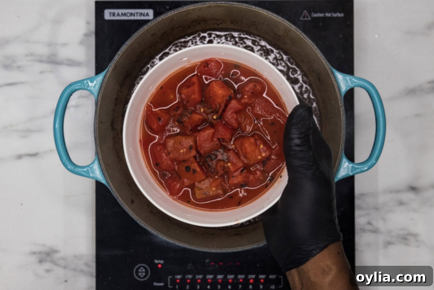 hand holding diced tomatoes in a bowl over dutch oven with braising liquid