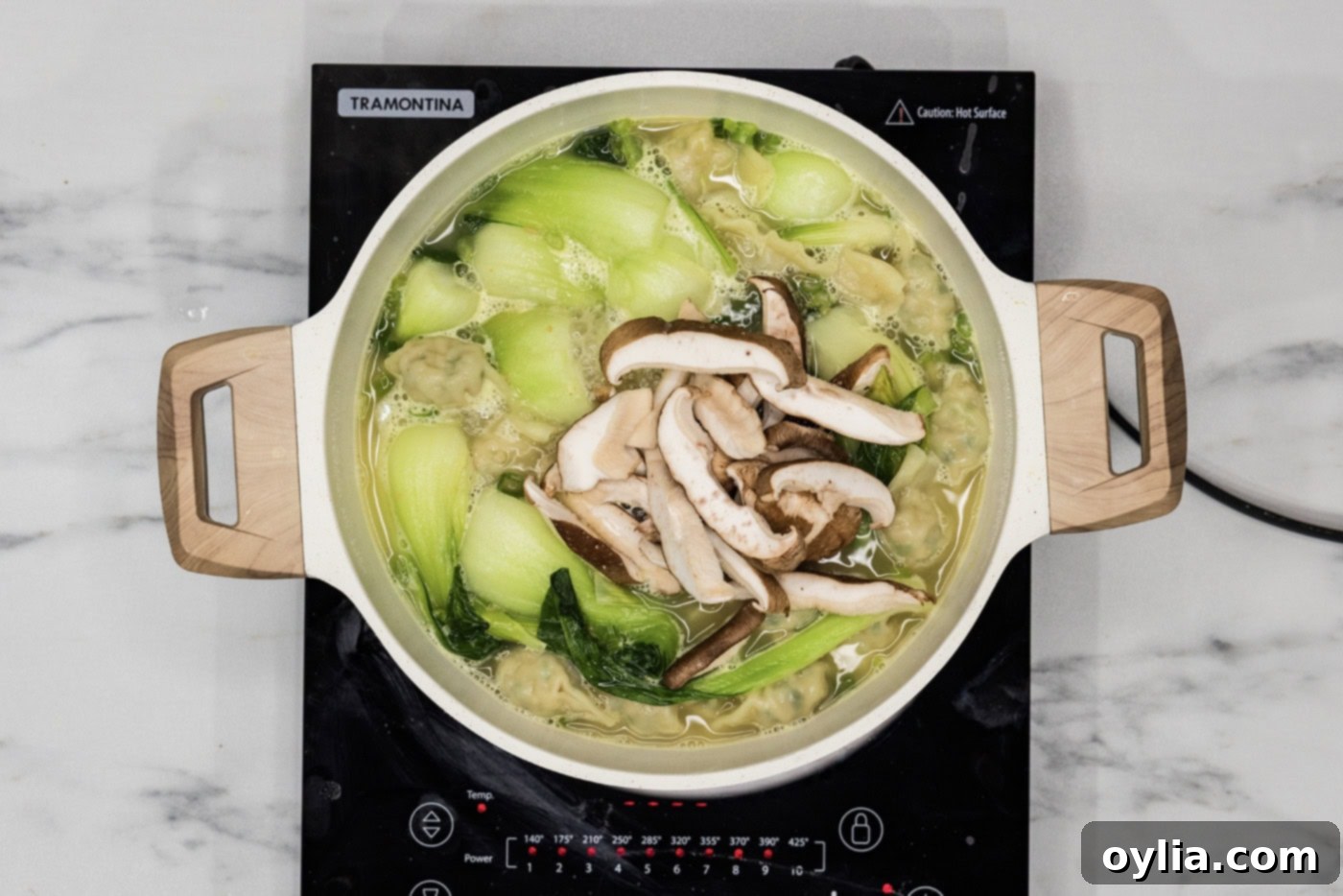 sliced shiitake mushrooms added to stockpot of wonton soup