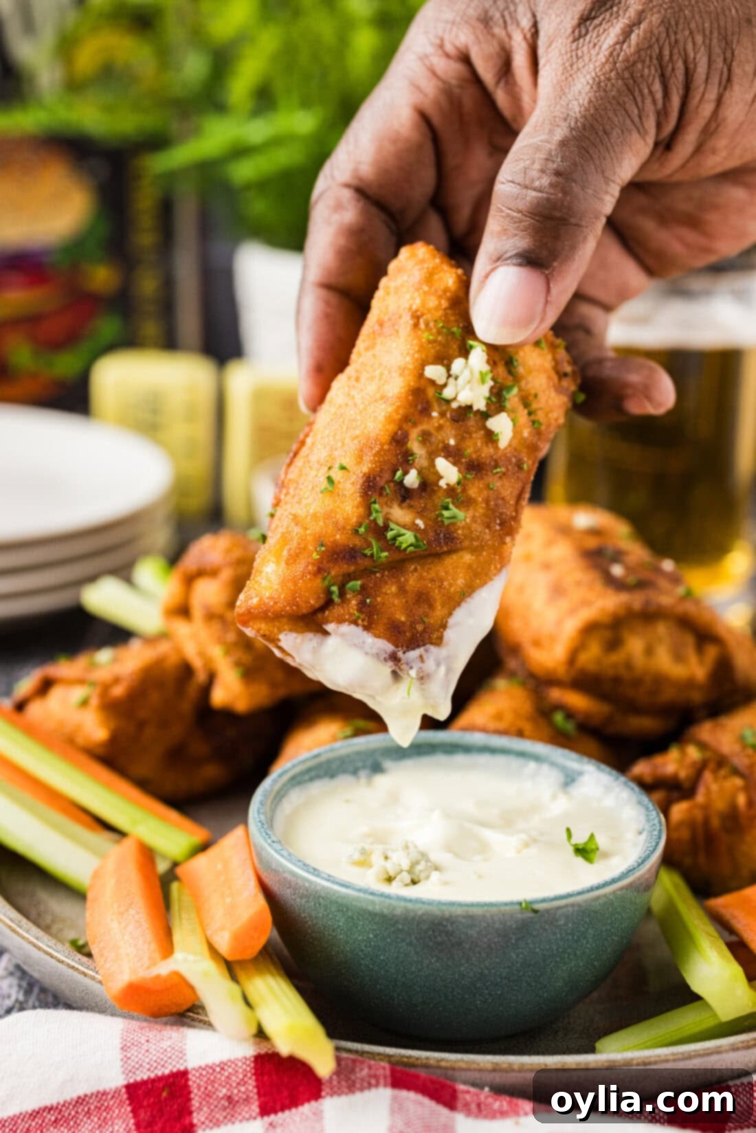 Hand holding a Buffalo Chicken Egg Roll dipped in creamy blue cheese dressing, showcasing its golden crispiness