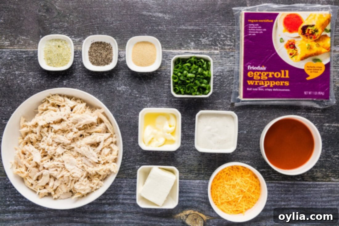 A selection of fresh ingredients laid out for making Buffalo Chicken Egg Rolls, including chicken, cheeses, sauces, and seasonings.