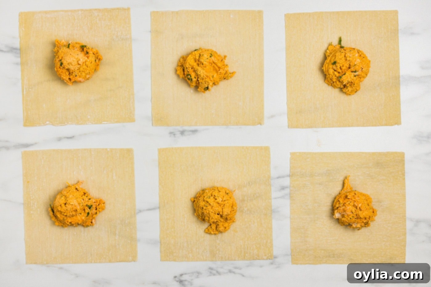 Egg roll wrappers laid out with a scoop of buffalo chicken mixture on each, ready for folding