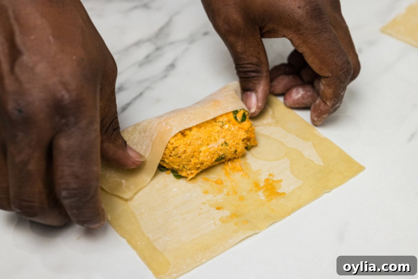 Hands demonstrating the folding process of a buffalo chicken egg roll